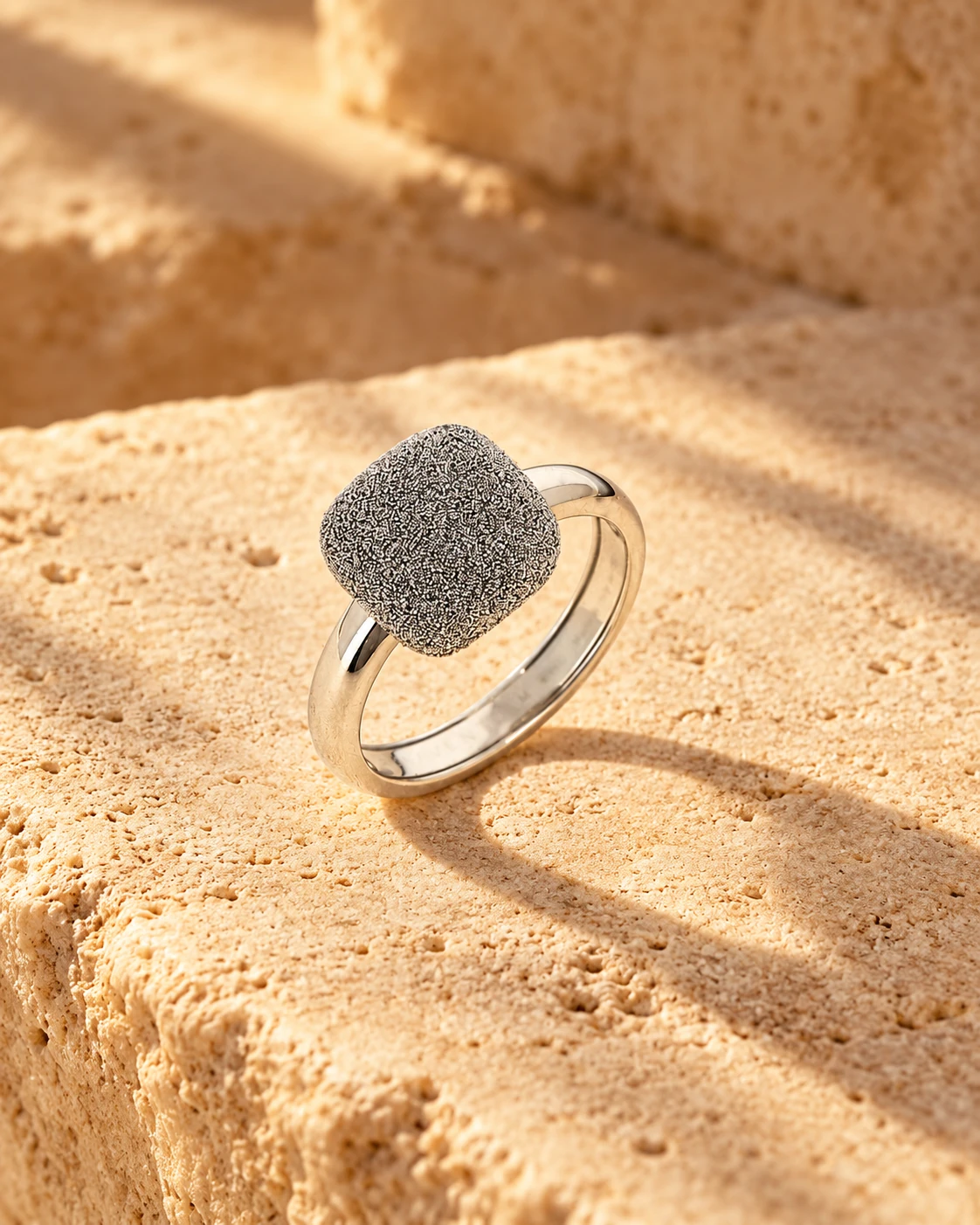 Anello Pesavento Cocktail con superficie grigia e montatura chiara su pietra color sabbia.